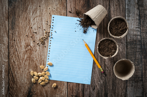 Closeup of peat planting pots filled with soil and seeds with sheet of blank paper to write shot on rustic wooden background. Gardening and planting seedlings, spring is here concept. Copyspace.