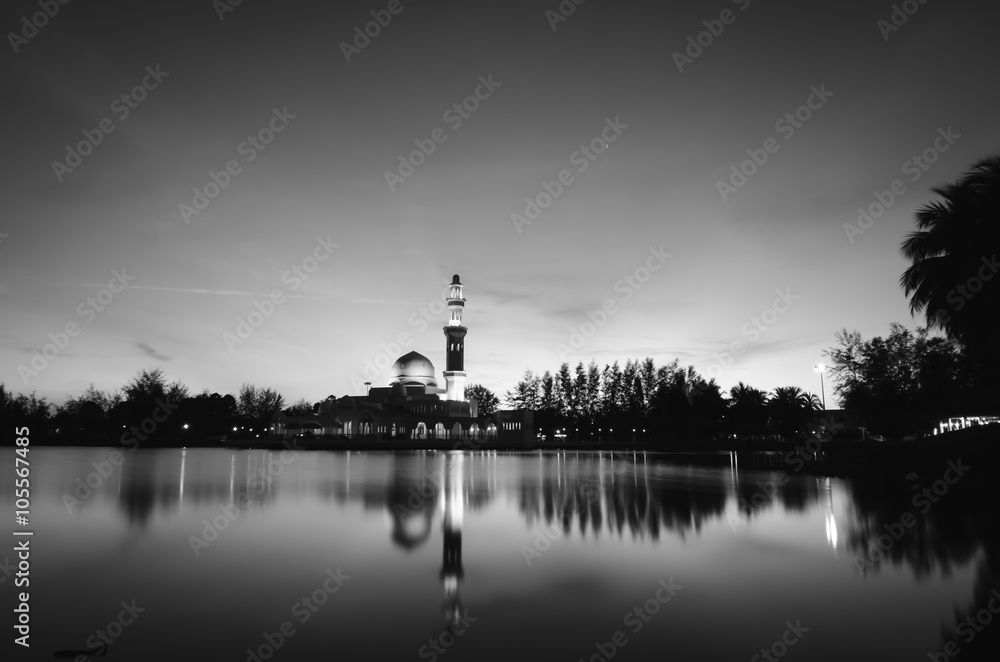 black and white concept of beautiful floating mosque on the lake surrounded by tree and coconut tree during sunset. soft on water with reflection