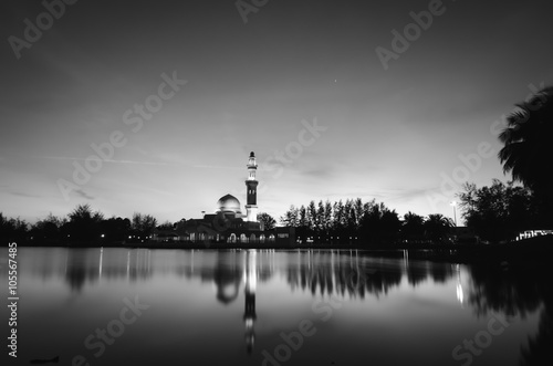 black and white concept of beautiful floating mosque on the lake surrounded by tree and coconut tree during sunset. soft on water with reflection