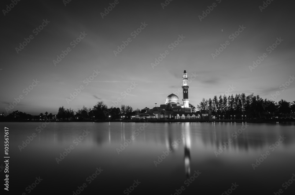 black and white concept of beautiful  mosque surrounded lake and coconut tree during sunset. soft focus on water with reflection