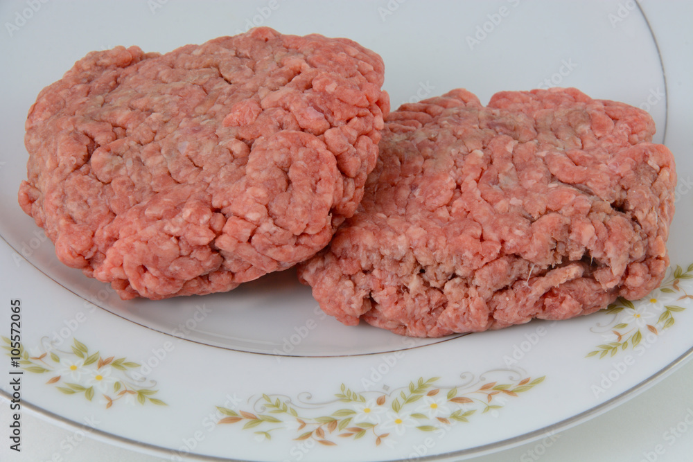 Two uncooked hamburger patties on plate in preparation of grilling or cooking Two uncooked hamburger patties on plate in preparation of grilling or cooking