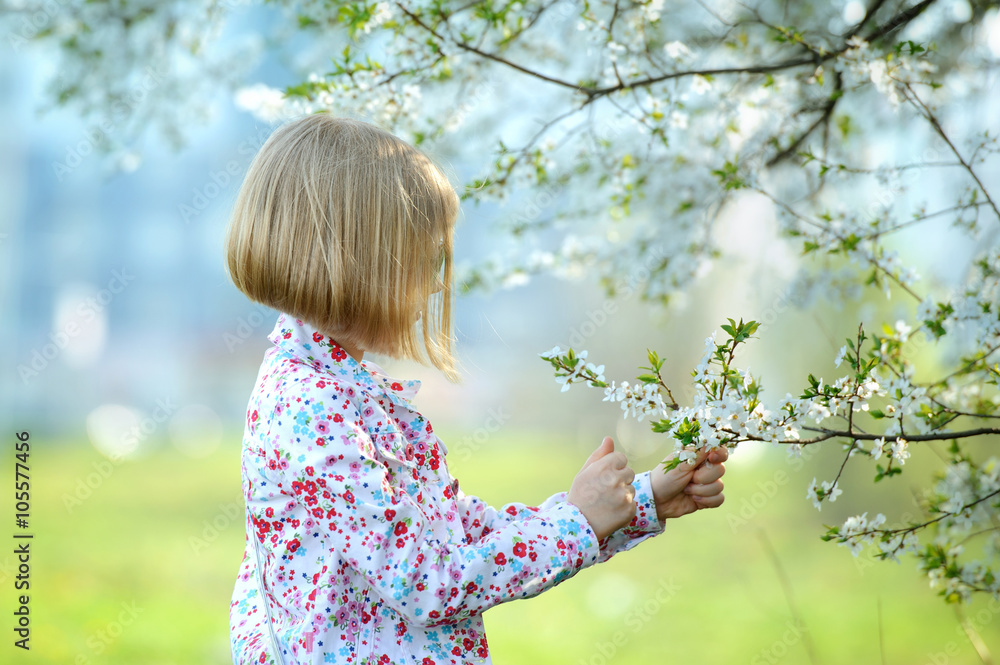 Beautiful happy little girl enjoying smell in a flowering sprin Beautiful happy little girl enjoying smell in a flowering sprin