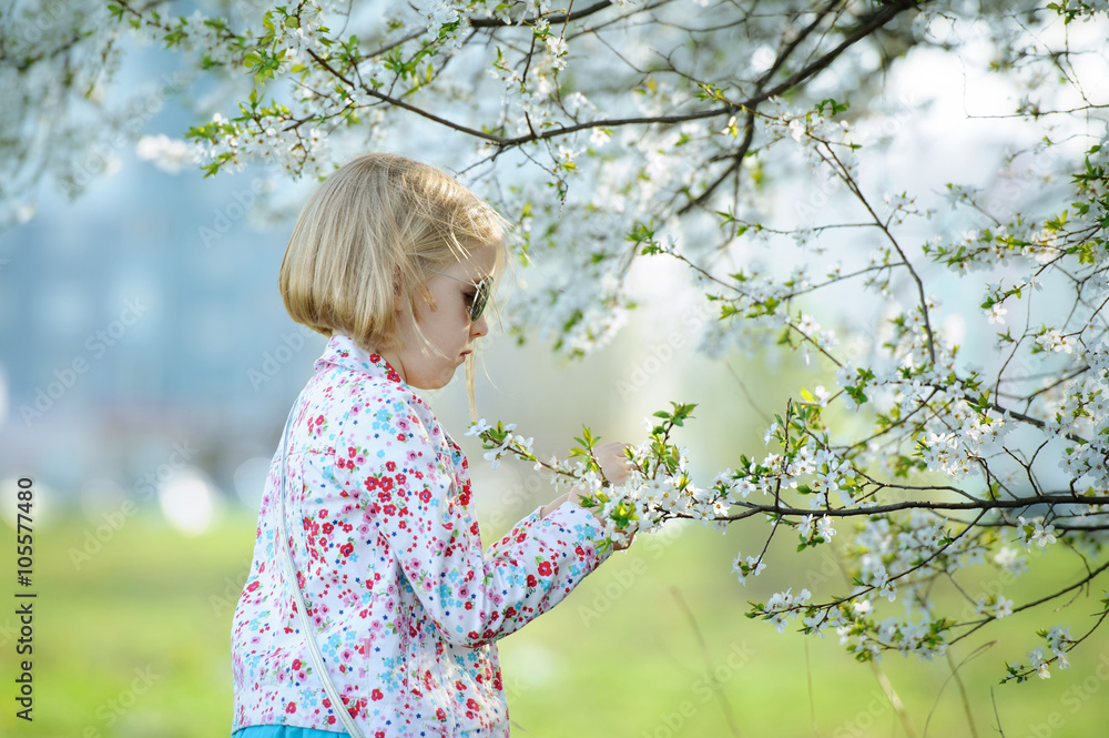 Beautiful happy little girl enjoying smell in a flowering sprin Beautiful happy little girl enjoying smell in a flowering sprin