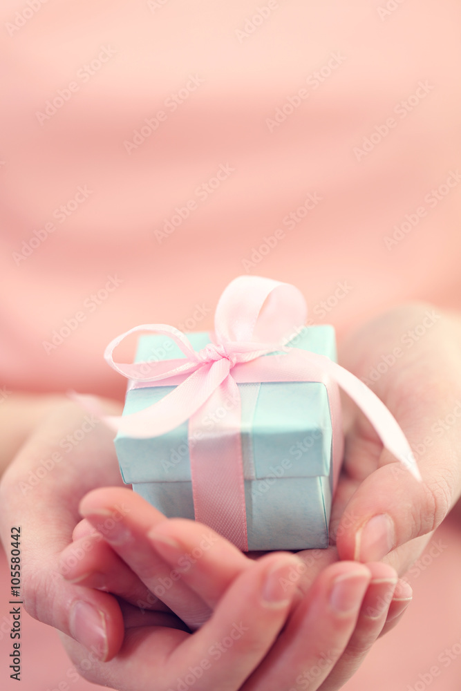 Female hands holding beautiful small gift wrapped with satin ribbon. Female hands holding beautiful small gift wrapped with satin ribbon.