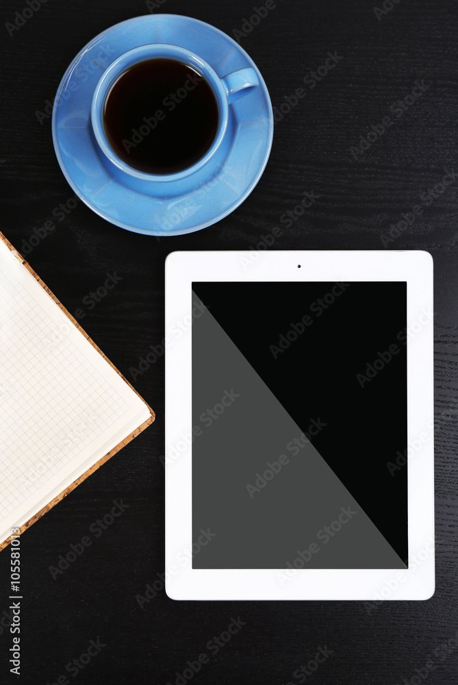 Tablet with cup of coffee and notepad on black wooden table Tablet with cup of coffee and notepad on black wooden table