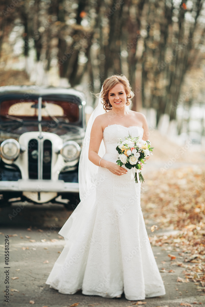 Beautiful happy bride with bouquet near retro car in autumn