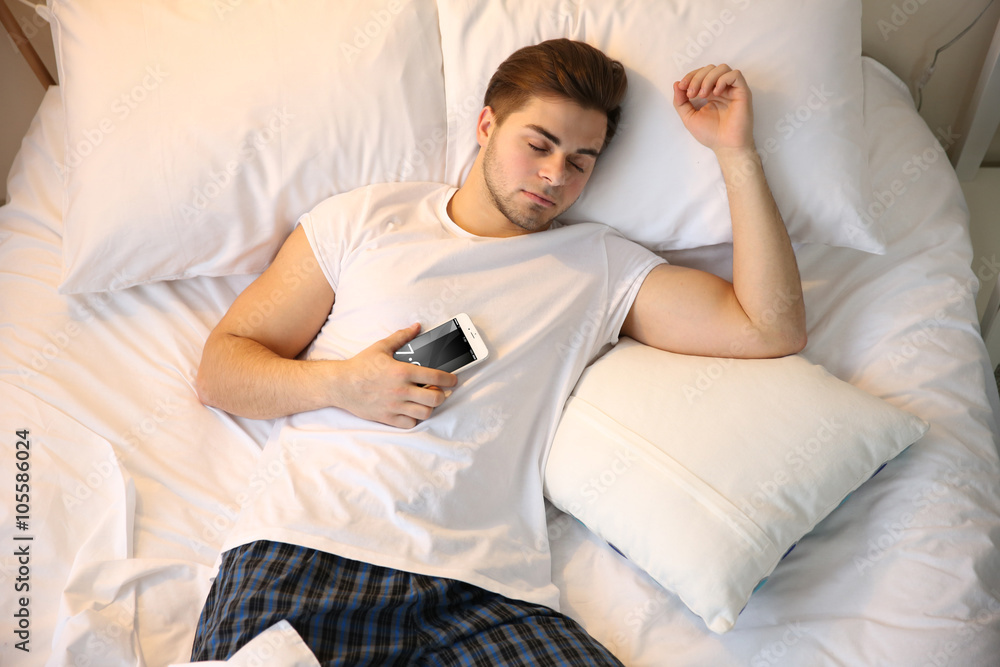 Young man sleeping with mobile phone in bed at home Young man sleeping with mobile phone in bed at home