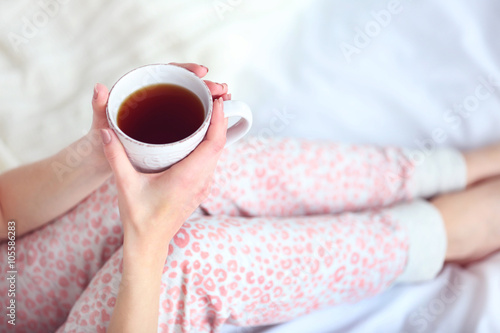 Attractive young blonde girl in a pajama sitting in white bedding and pillows