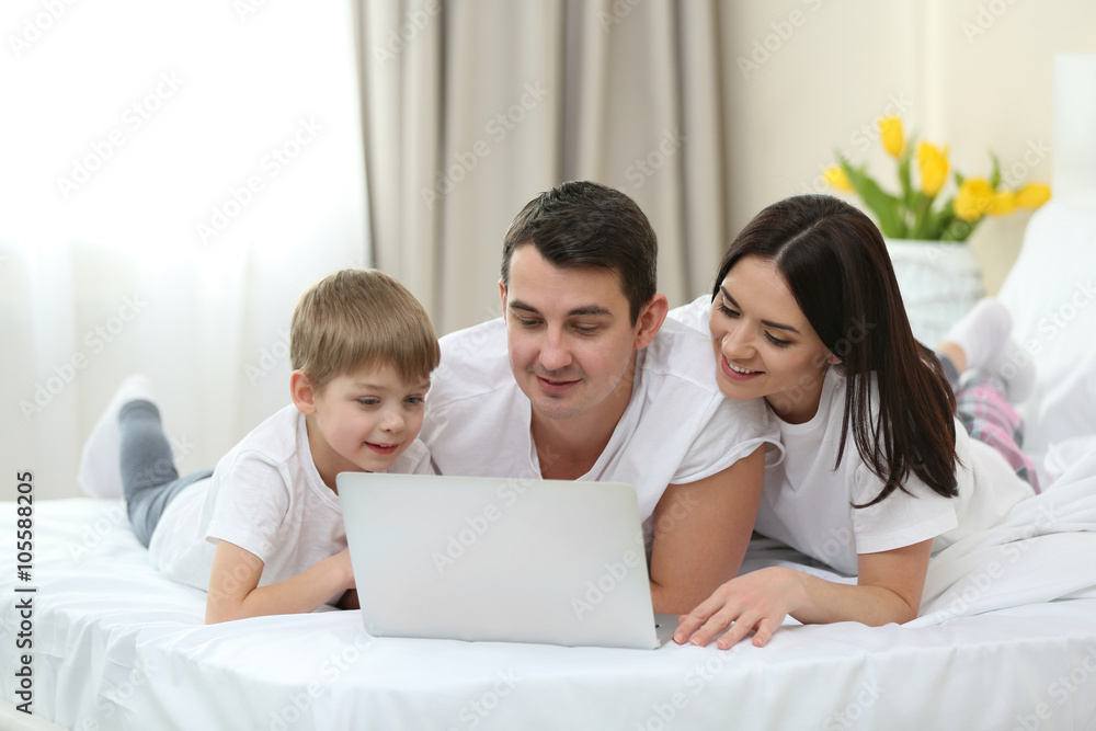 Fototapeta premium Family with laptop lying in bed