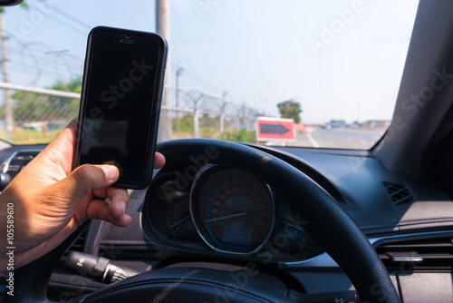 Man's hands of a driver on steering wheel and on mobile phone