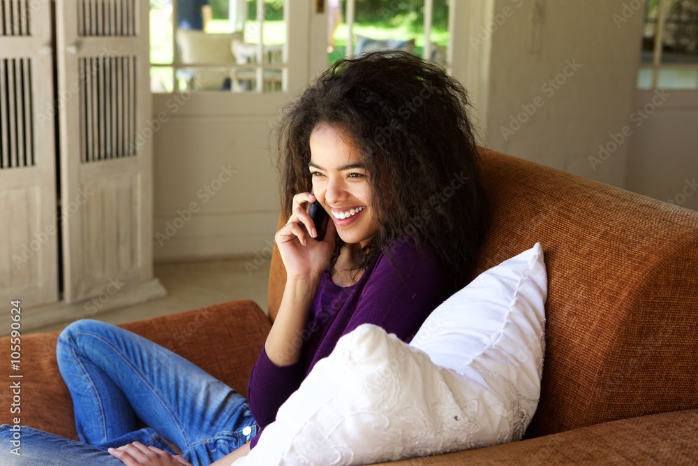 Smiling young woman sitting on couch talking on mobile phone Smiling young woman sitting on couch talking on mobile phone