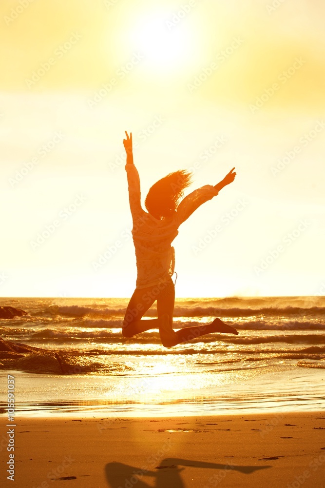 Sunset portrait young woman jumping for joy at the beach