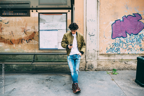 Young handsome caucasian man leaning on a bus stop holding a sma photo