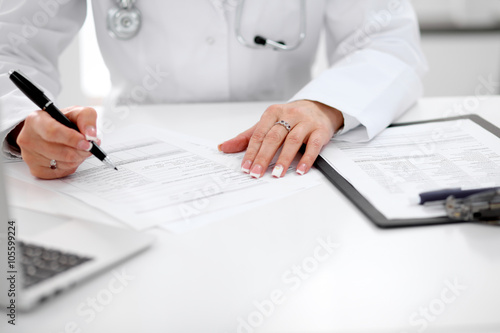 Close-up of a female doctor filling out application form , sitting at the table in the hospital