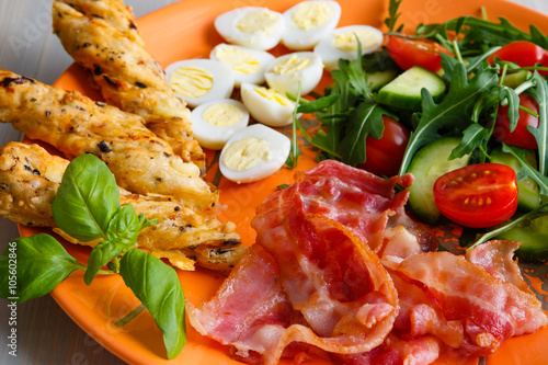 Traditional english breakfast egg, bacon, salad, homemade bread and basil