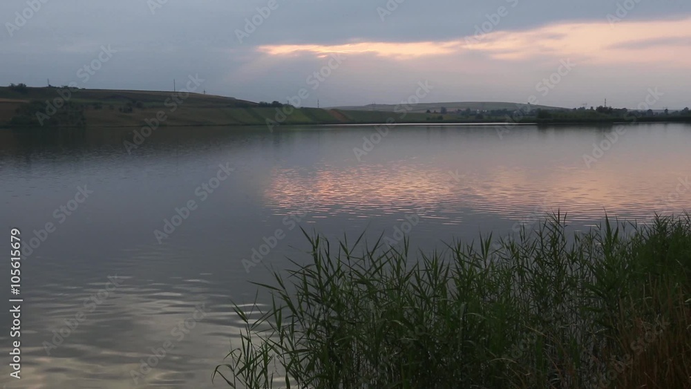 Evening lake scenery with sun reflection on water surface and reeds in front.
Evening lake scenery with sun reflection on water surface and reeds in front.