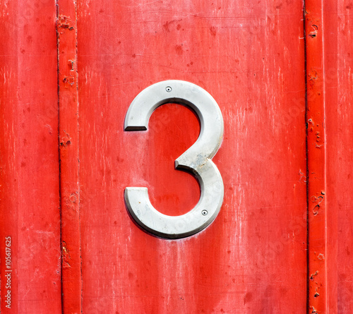 White number 3 sign on a red wooden door