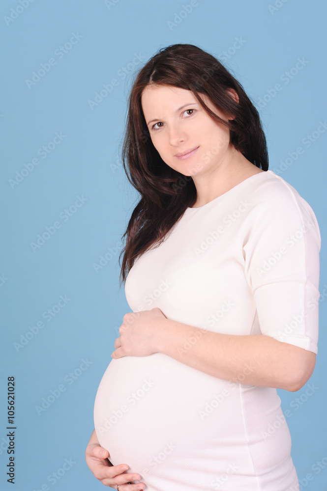 Smiling young pregnant woman holding belly on blue background Smiling young pregnant woman holding belly on blue background