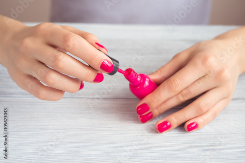 Women s hands with a red manicure open a bottle of varnish