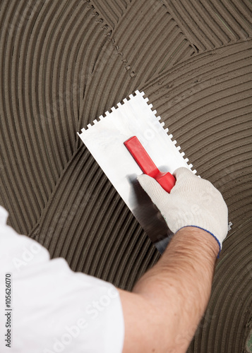 the worker applies glue for a tile on a wall