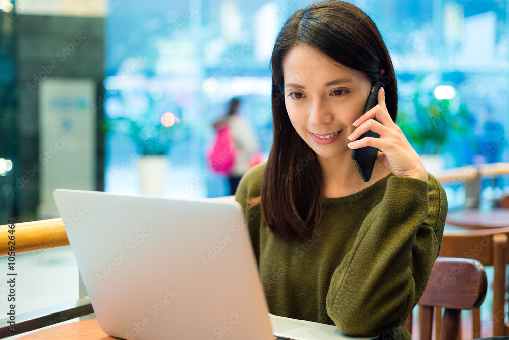 Woman talk to cellphone with use of laptop computer in coffee sh Woman talk to cellphone with use of laptop computer in coffee sh