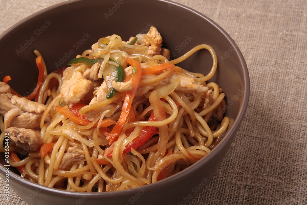 Stir fried noodle with chicken and vegetables in brown plate wit Stir fried noodle with chicken and vegetables in brown plate wit