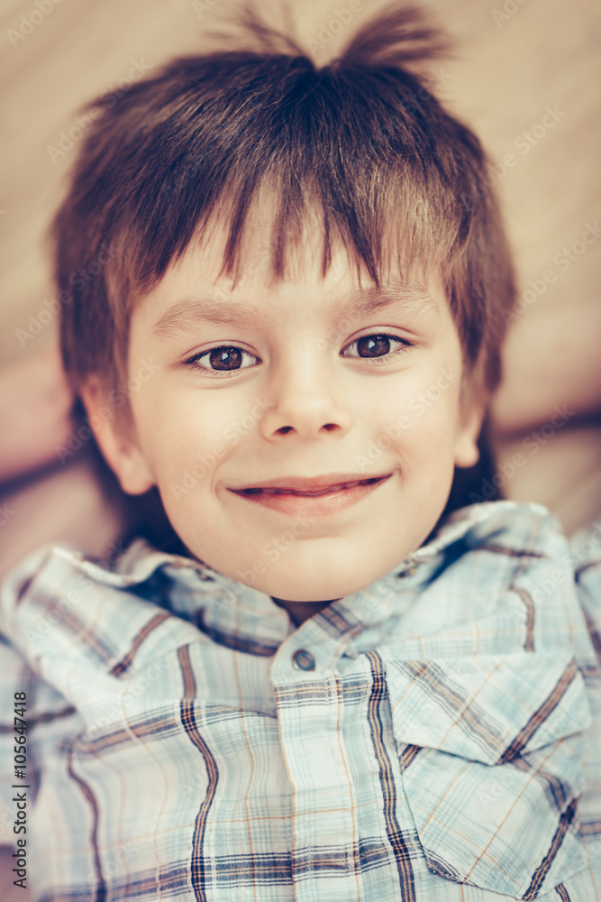 Closeup portrait of smiling little boy with brown eyes wearing checkered shirt lying on floor and looking at camera. Happy childhood concept, selective focus on eyes, top view, instagram filters Closeup portrait of smiling little boy with brown eyes wearing checkered shirt lying on floor and looking at camera. Happy childhood concept, selective focus on eyes, top view, instagram filters