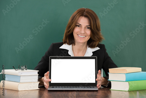 Female Teacher With Laptop Sitting At Classroom Desk