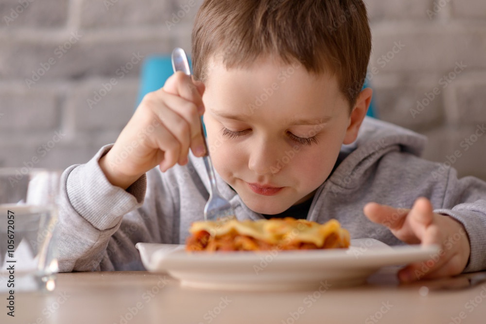 7 years old boy eating lasagne in dining room 7 years old boy eating lasagne in dining room