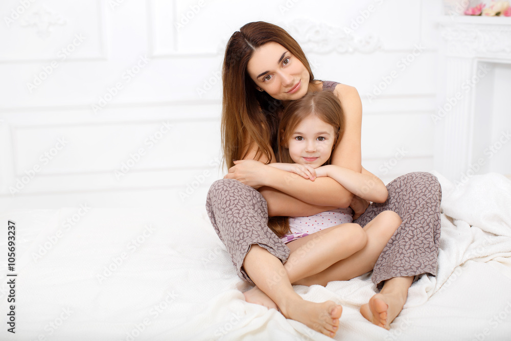 The girl and her mother sitting on a white bed in the bedroom The girl and her mother sitting on a white bed in the bedroom