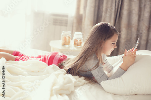 Cute little girl working with tablet computer lying in bed