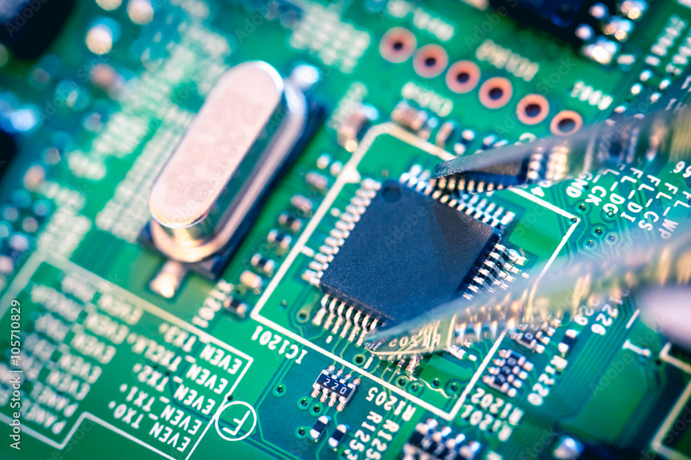 Close up on tweezers holding a microchip on computer motherboard. Close up on tweezers holding a microchip on computer motherboard.