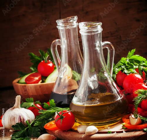 Olive oil and balsamic vinegar in pitchers, vegetables, herbs an