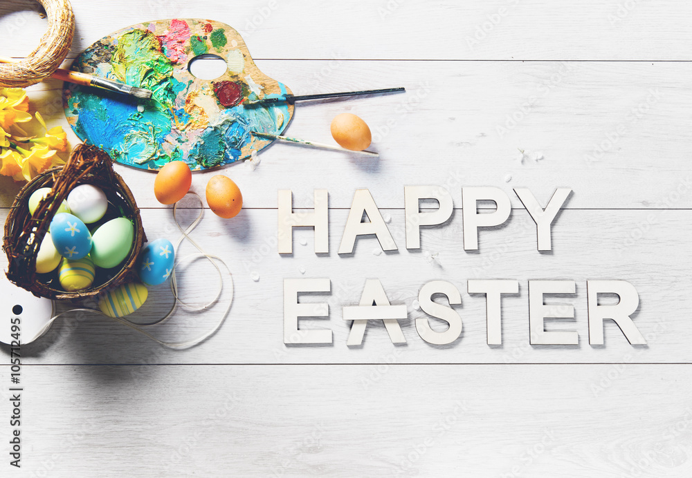Colored eggs and other decorations on a white wooden table with HAPPY