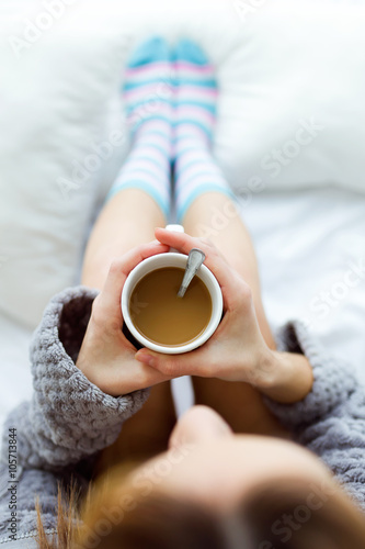 Beautiful young woman drinking coffee on bed.