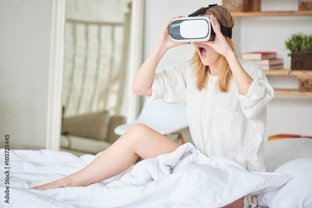 The girl in white sitting on the bed in the virtual reality helmet The girl in white sitting on the bed in the virtual reality helmet