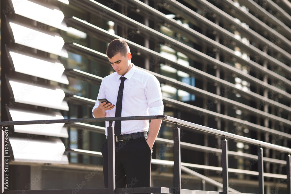 Handsome young businessmen using phone while standing in front of the modern office building Handsome young businessmen using phone while standing in front of the modern office building
