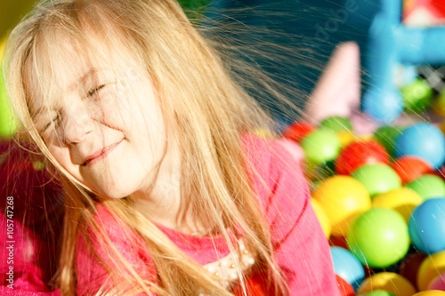 Little smiling girl playing lying in colorful balls park playground photo