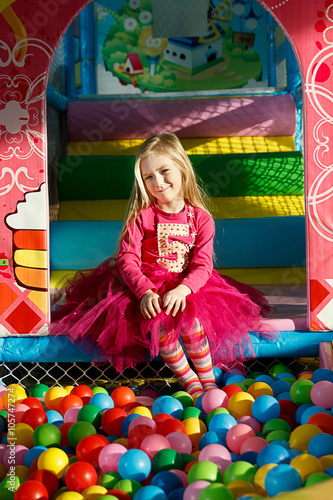 Little smiling girl playing lying in colorful balls park playground photo