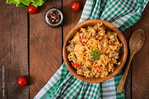 Bulgur with chicken, mushrooms and tomatoes in a wooden bowl. Top view