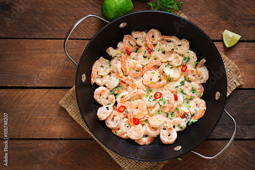 Shrimp in a creamy garlic sauce with parsley and lime in a frying pan. Top view
