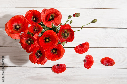 Fototapeta Naklejka Na Ścianę i Meble -  Bouquet of red poppies in glass vase and poppy petals near on ol