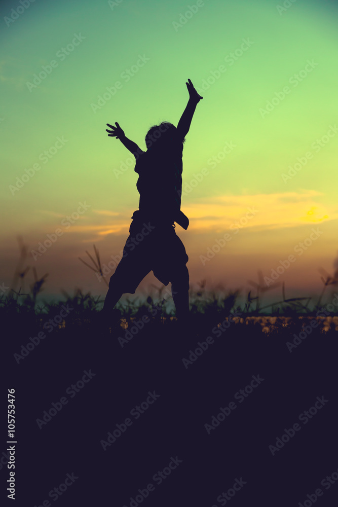 Silhouette of child jumping against sunset. Boy enjoying the view