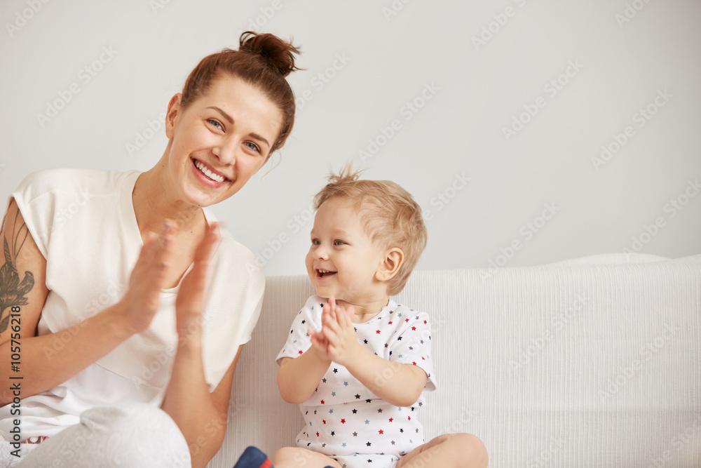 Young mother playing with her little baby on the bed - indoors