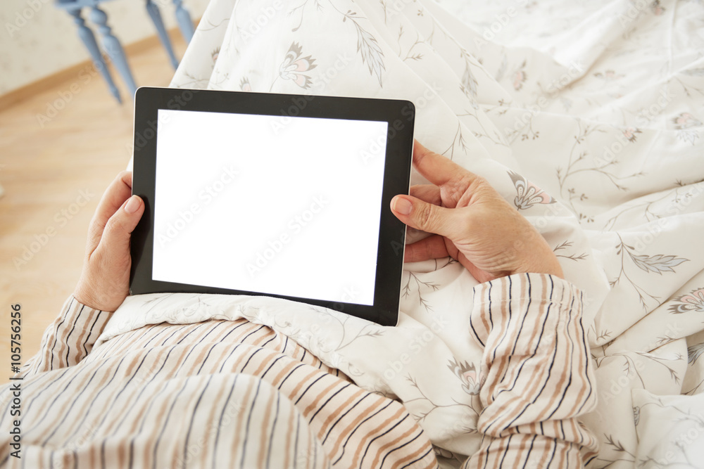 Close up to view mature woman's hands hold black tablet with empty screen, female hands holding touch screen tablet pc with blanc screen lying on her bed in a bedroom.