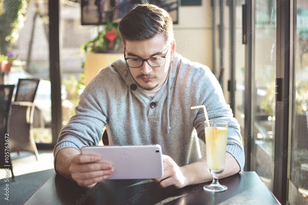 Young handsome contemporary businessman seated on a bar using a tablet and a notebook looking in camera - business, work, study, technology concept Young handsome contemporary businessman seated on a bar using a tablet and a notebook looking in camera - business, work, study, technology concept