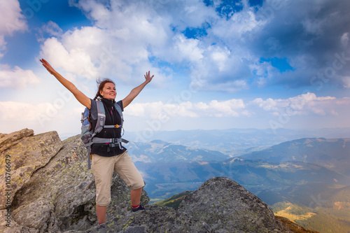 Young happy woman with backpack standing on top of the mountain.