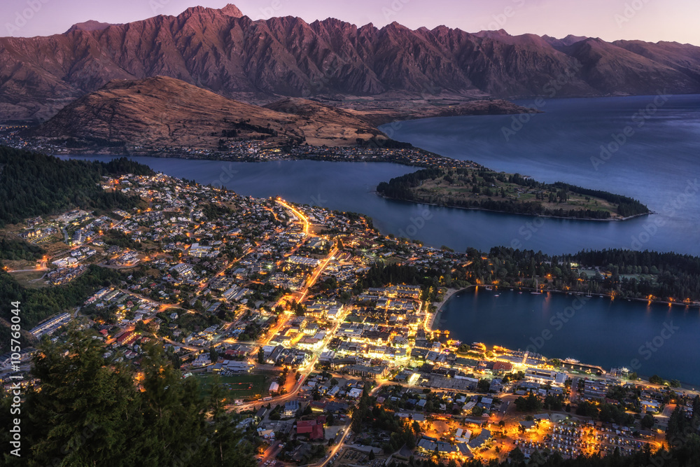 sunset view over queenstown in new zealand taken when the city is still lit up with lake wakatipu in the distance.