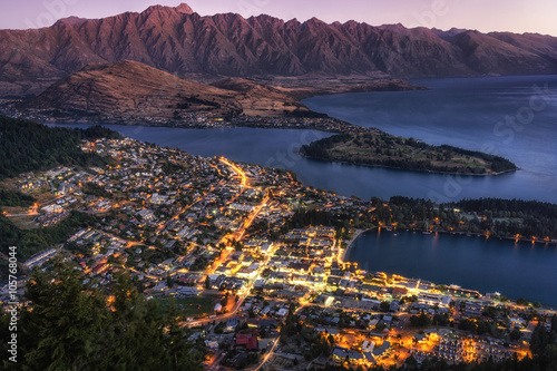 sunset view over queenstown in new zealand taken when the city is still lit up with lake wakatipu in the distance.