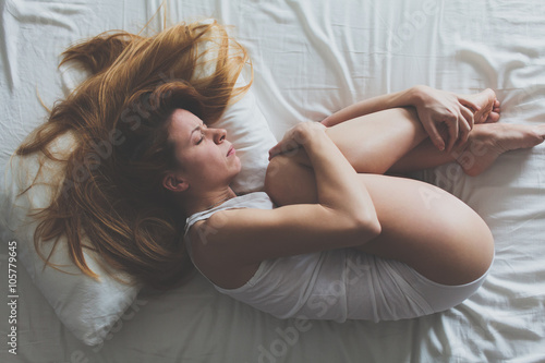 Young woman lying down on the bed in fetus position photo
